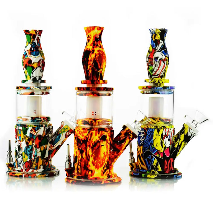 Three 10-inch water pipes with silicone bases and necks, and clear glass chambers, displayed against a white background. The left pipe features a colorful skull and cartoon pattern, the middle one has a vibrant red and orange flame design, and the right one showcases a yellow, blue, and red pop art cartoon motif.