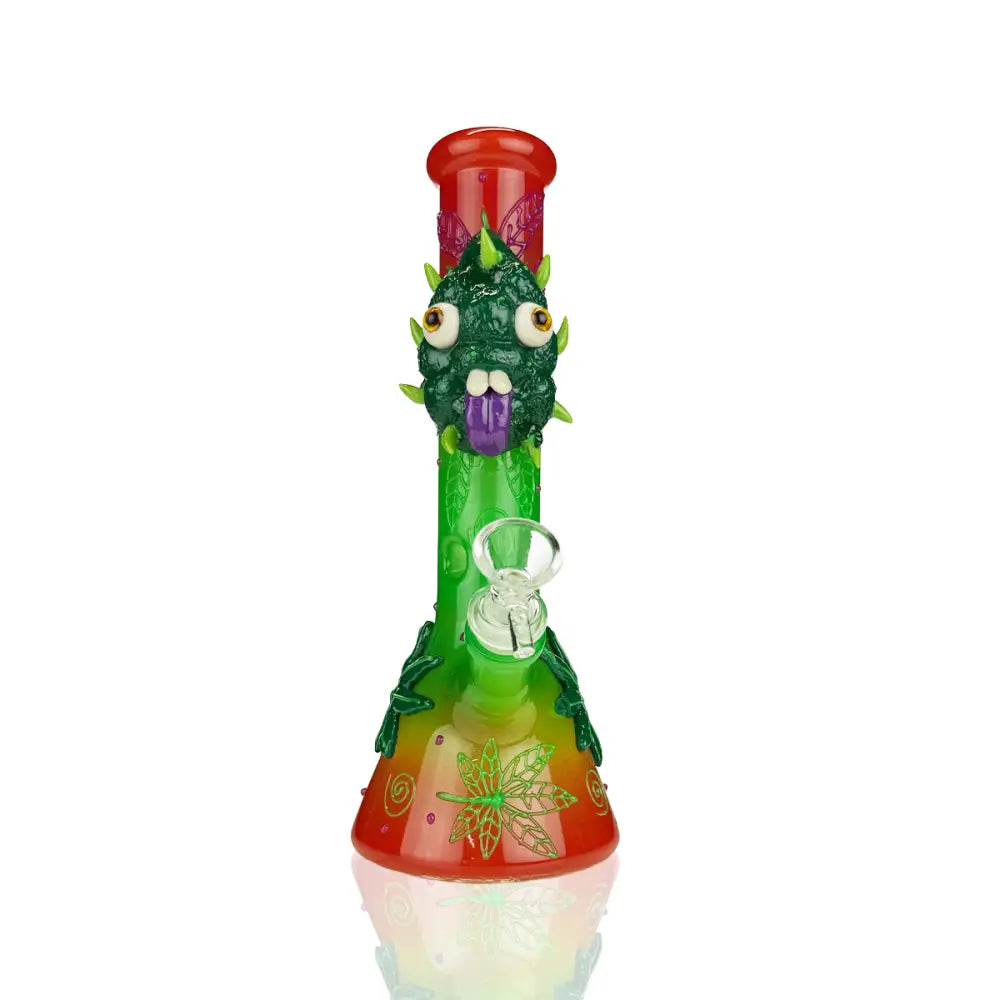 A vibrant green and red glass beaker water pipe featuring a monster-like face with bulging eyes and a purple tongue, adorned with cannabis leaf designs.
