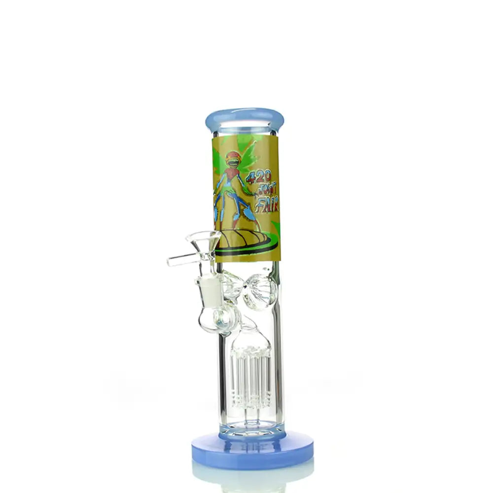 A clear glass straight tube water pipe with a light blue base and mouthpiece, featuring a yellow and green graphic on the neck that reads '420 SMOKE FAIR' with cartoon figures. A clear glass percolator is visible inside, and a 14mm male bowl is attached to the side.