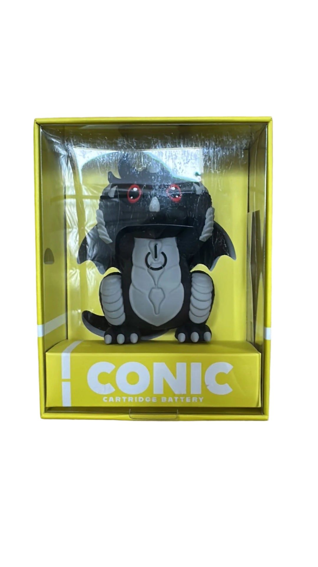 A black dragon-shaped vape battery with red eyes and a light gray belly, displayed upright in its clear plastic and yellow cardboard packaging. The packaging features the text 'iCONIC CARTRIDGE BATTERY'.
