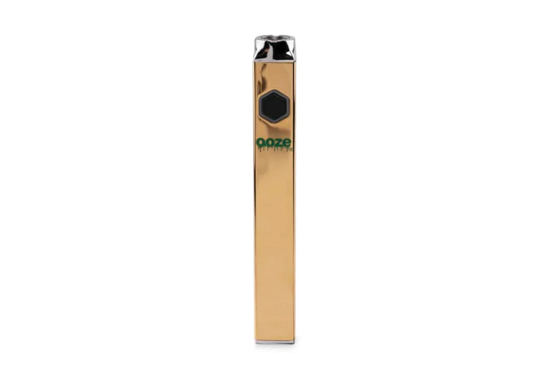 A sleek, rectangular gold vaporizer battery stands upright against a white background, featuring a black hexagonal button and green 'ooze QUAD' branding.