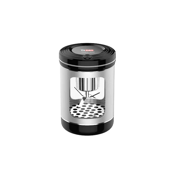 A cylindrical dry herb grinder with a metallic silver body, black top and base, and a clear window revealing internal blades and a perforated bottom.