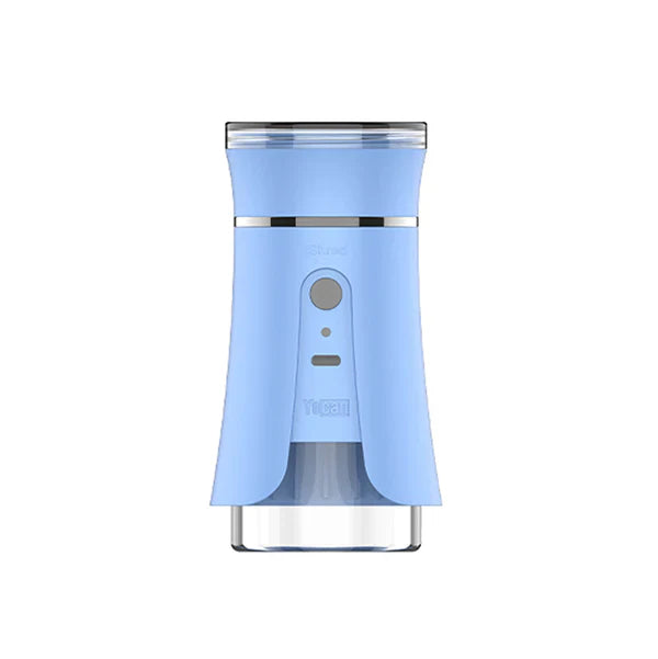 Close-up detail shot of a light blue electric dry herb grinder with a silver button and clear bottom section, featuring the 'Yocan' brand name.