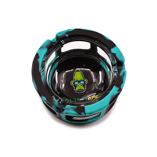 Top-down view of a round ashtray with a teal and black camouflage-patterned silicone sleeve, featuring a green ape head logo in the center.