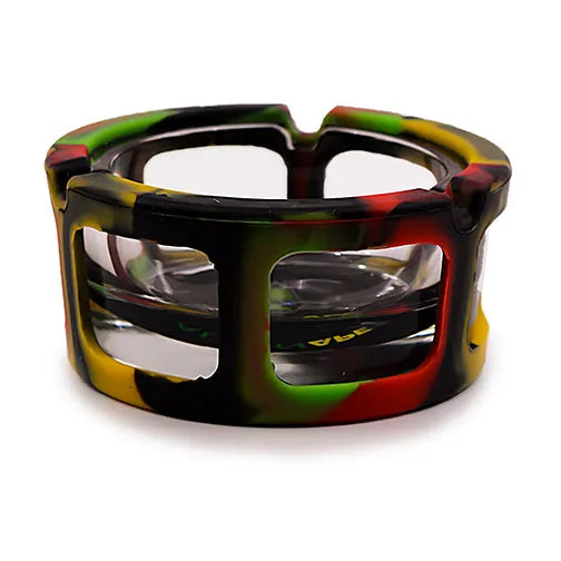 A round glass ashtray encased in a multi-colored silicone sleeve, featuring black, red, green, and yellow in a camouflage-like pattern. The ashtray has multiple cigarette rests along its rim. This is a clear product shot on a white background.