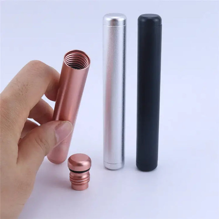 A hand holds an open rose gold aluminum pre-roll tube, revealing internal threading, next to closed silver and black tubes on a white surface.