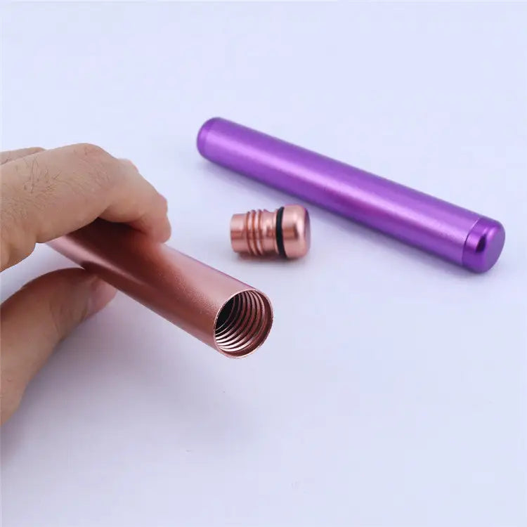 Detail shot of a rose gold aluminum tube held by a hand, showing its threaded opening, next to a matching threaded cap and a closed purple tube.