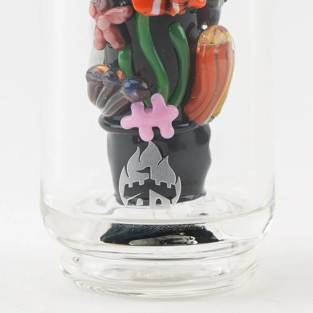 Detail shot of a glass attachment base, black with a silver logo, surrounded by colorful glass marine life decorations, including a pink jigsaw puzzle piece.