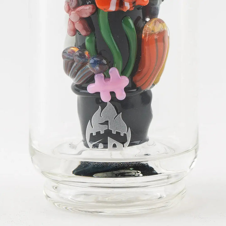 Detail shot of a glass attachment base, black with a silver logo, surrounded by colorful glass marine life decorations, including a pink jigsaw puzzle piece.