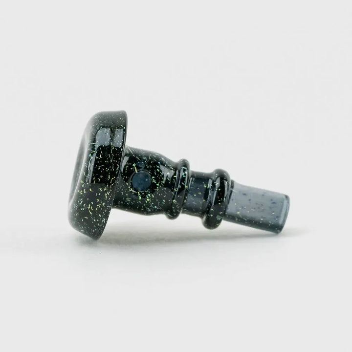Close-up side view of a black glass accessory with green and gold glitter-like speckles, featuring a wider flat end and a narrower tapered end with two raised rings.