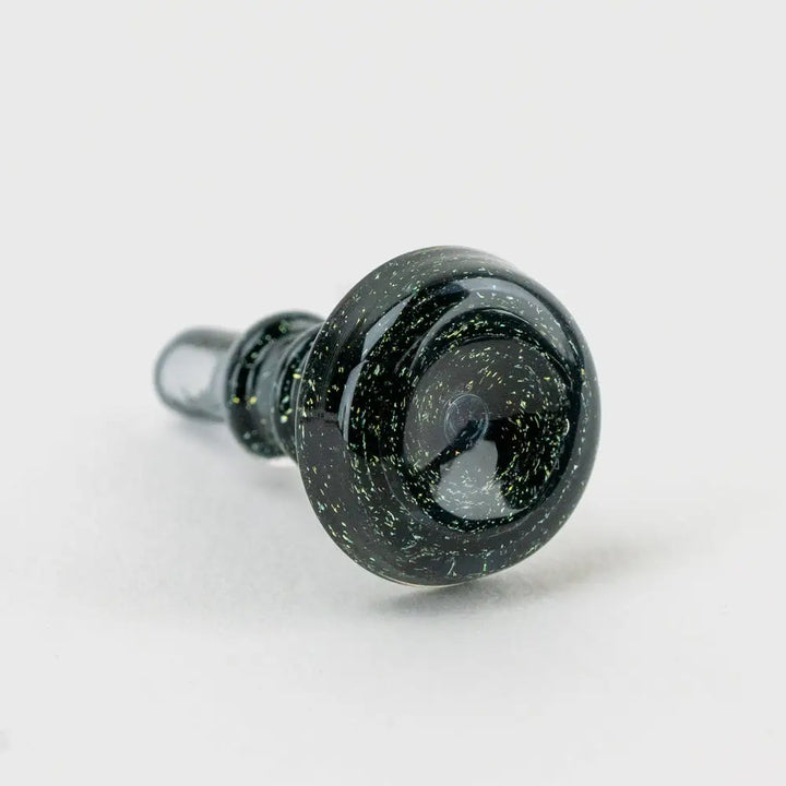 Close-up, angled view of a black glass accessory with sparkling green and yellow speckles, highlighting its textured surface and bowl shape.