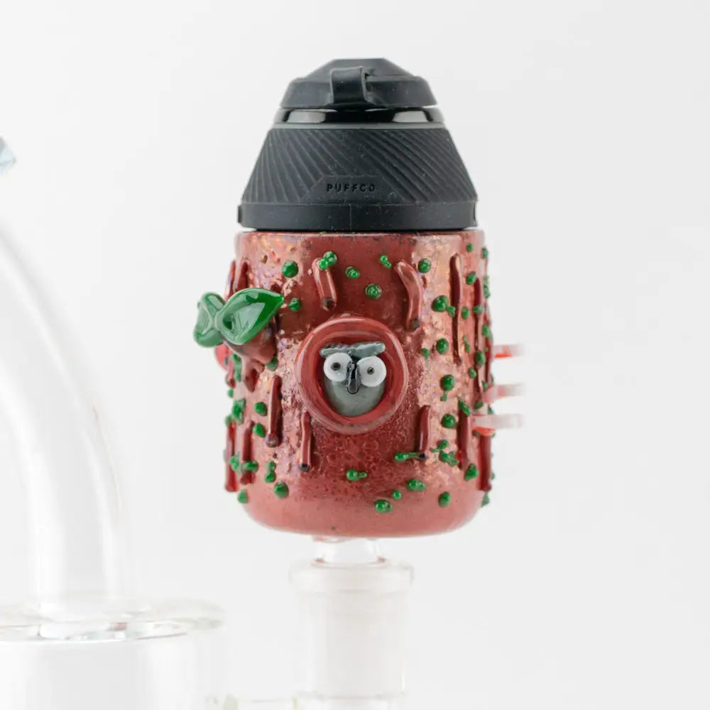 Close-up detail of a Puffco Proxy attachment shaped like a reddish-brown tree stump with green moss and a small owl peeking from a hole.