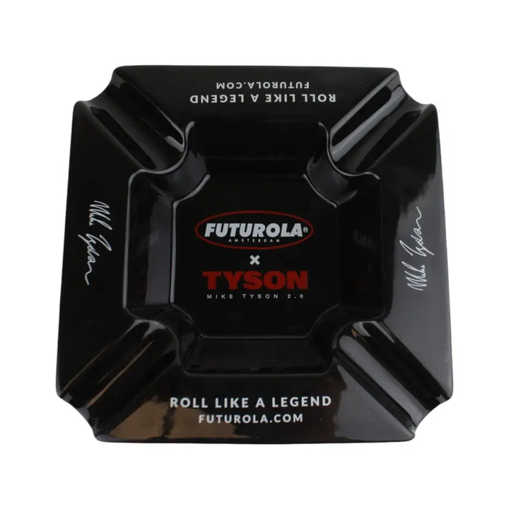 A black, square ashtray with rounded corners and four cigar rests. It features a red and white 'FUTUROLA AMSTERDAM' logo, a red 'TYSON' logo, and 'MIKE TYSON 2.0' text in the center. The phrases 'ROLL LIKE A LEGEND' and 'FUTUROLA.COM' are printed on two sides, and a white signature is on the other two sides.