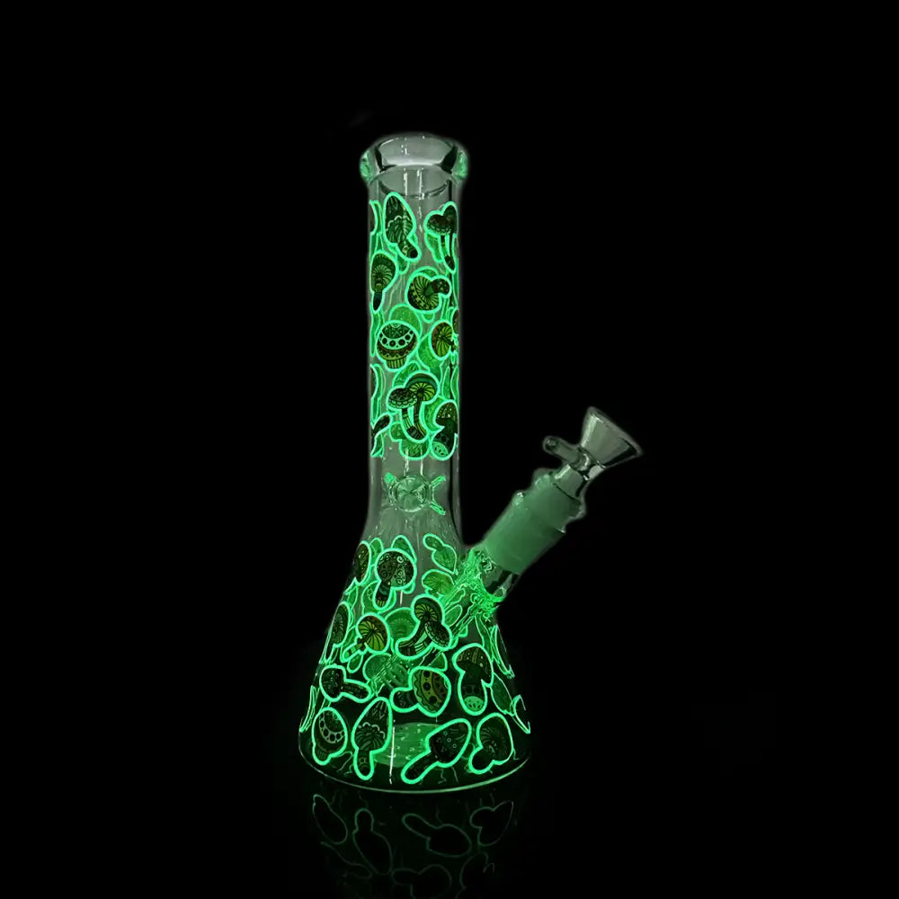 A full view of a glow-in-the-dark beaker-shaped water pipe, featuring a vibrant green mushroom pattern against a dark background, with a glass bowl piece attached.