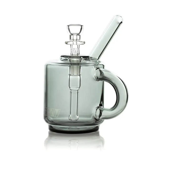 A small, smoky grey glass bubbler shaped like a coffee mug with a handle, featuring a clear glass downstem and a bowl piece on top, set against a white background.