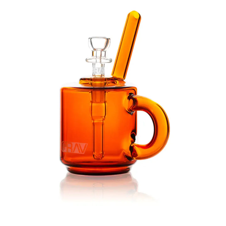 Front view of an orange glass bubbler designed like a coffee mug, featuring a clear glass bowl, an angled mouthpiece, and a handle on the right side. The 'GRAV' logo is visible on the front.