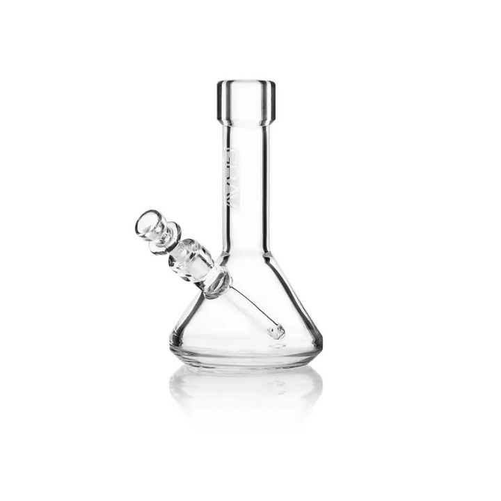 A clear glass beaker-style water pipe with a removable downstem and bowl, reflecting on a clean white surface.