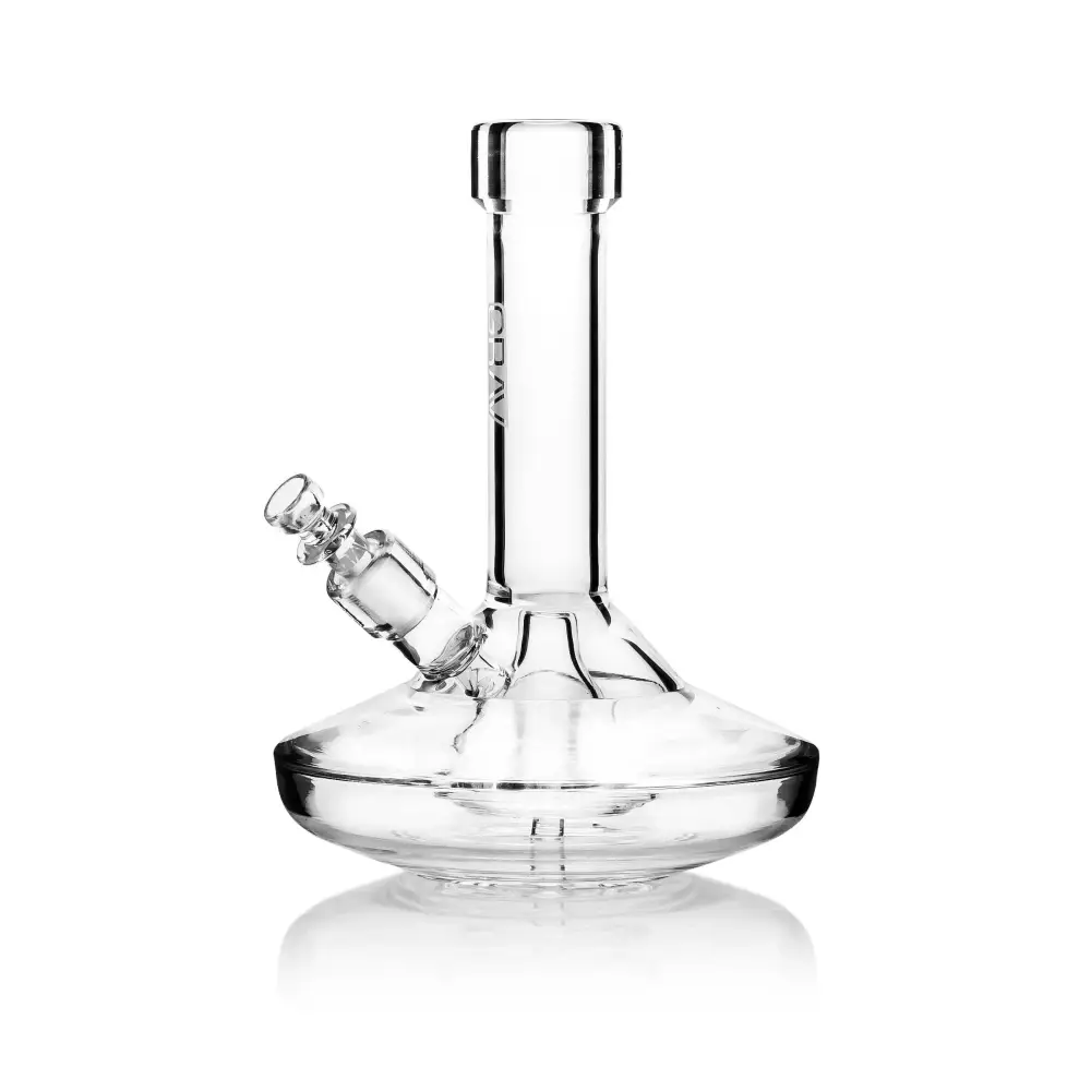 A clear glass water pipe with a wide, flat circular base and a straight neck, featuring an angled downstem and bowl, presented on a reflective white background.