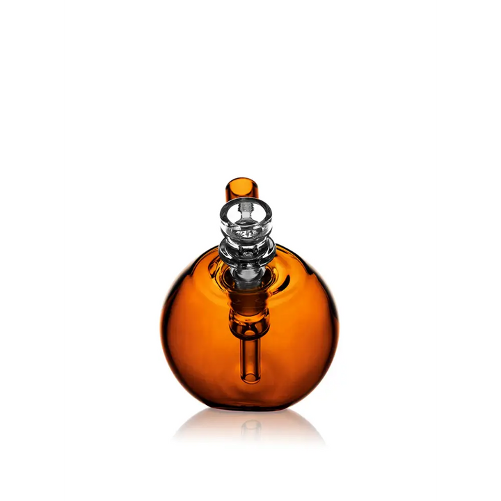 A spherical amber glass pocket bubbler with a clear glass mouthpiece and downstem, reflecting on a white surface.