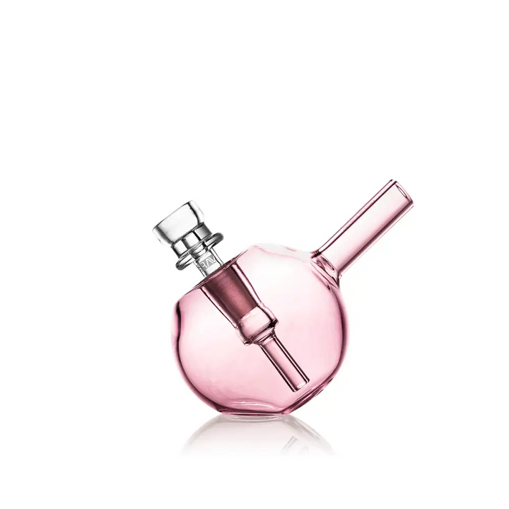 A compact, spherical pink glass bubbler with a clear glass bowl and downstem, shown at an angle with a reflection on a white surface.