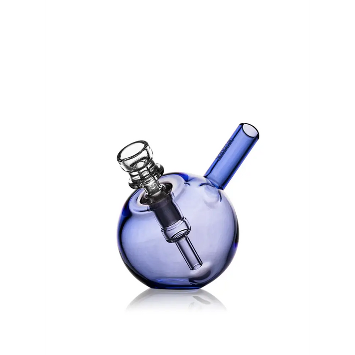 A compact, spherical blue glass bubbler with a clear glass downstem and bowl, angled slightly to the right on a reflective white surface.