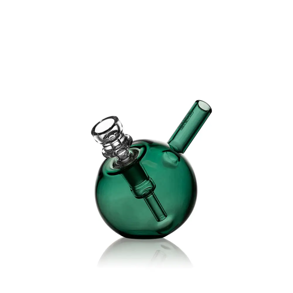 A compact, spherical green glass bubbler with a clear glass bowl and mouthpiece, reflecting on a white surface.