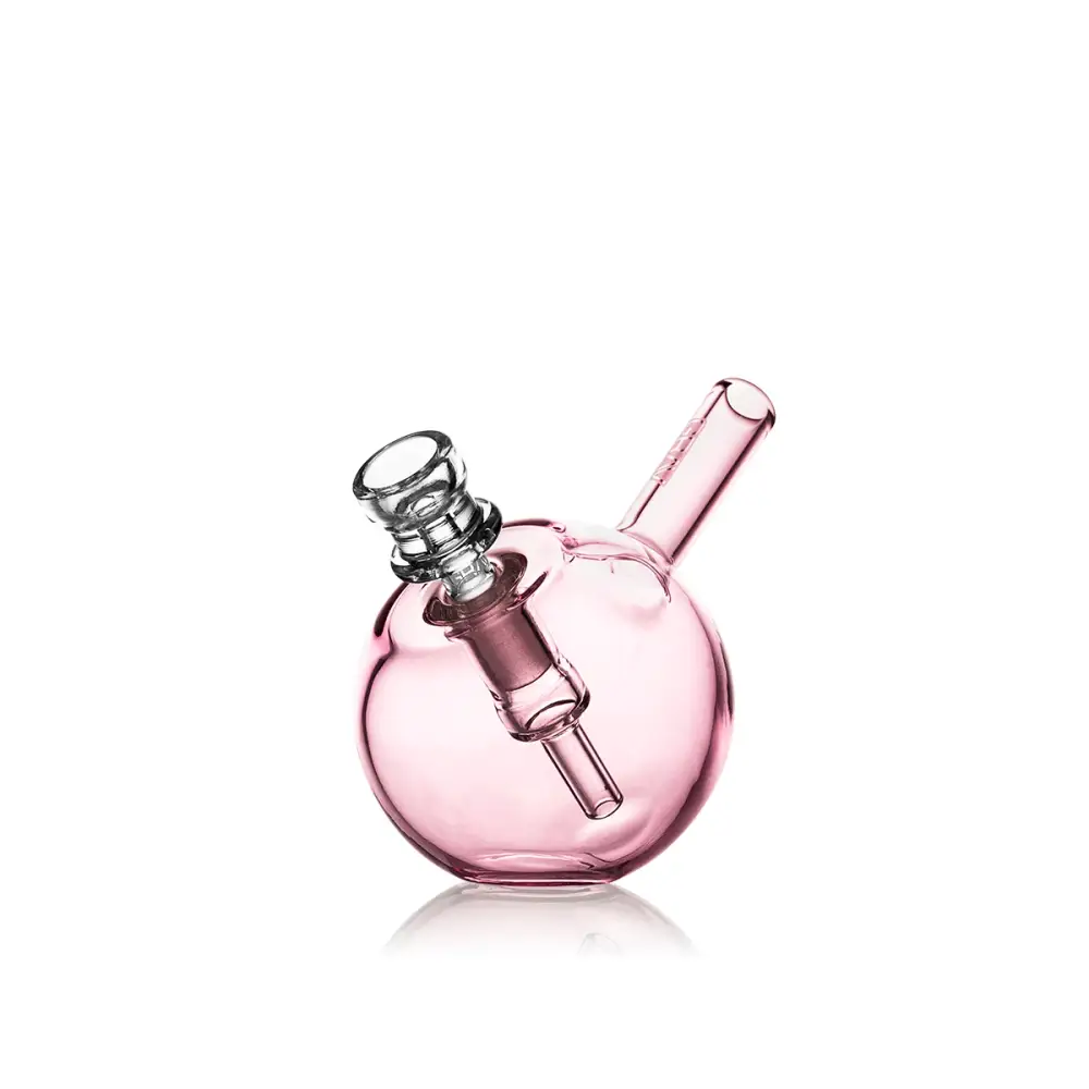A small, spherical pink glass bubbler with a clear glass bowl and downstem, angled slightly to the right on a reflective white surface.