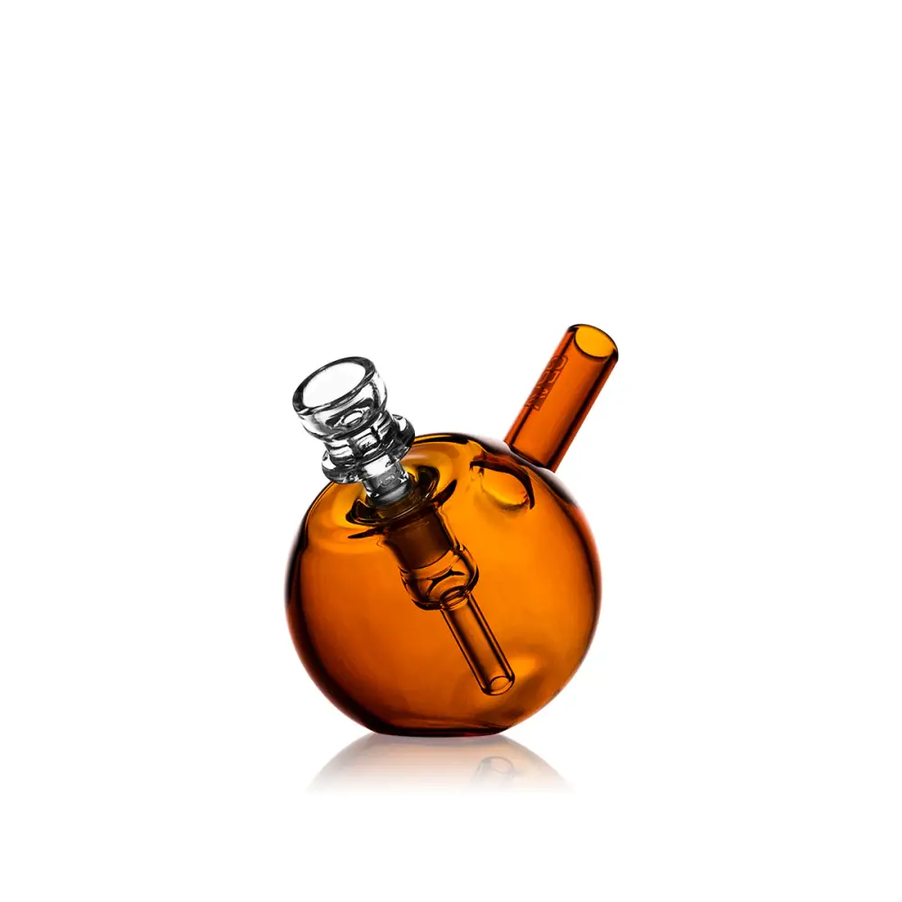 Full view of a compact amber spherical glass bubbler with a clear glass bowl and mouthpiece, reflecting on a white surface.