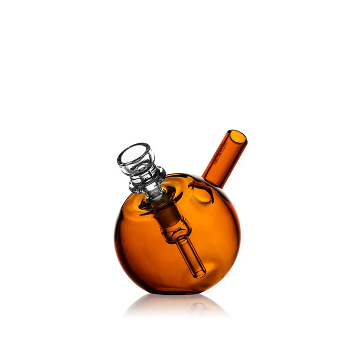 Full view of a compact amber spherical glass bubbler with a clear glass bowl and mouthpiece, reflecting on a white surface.