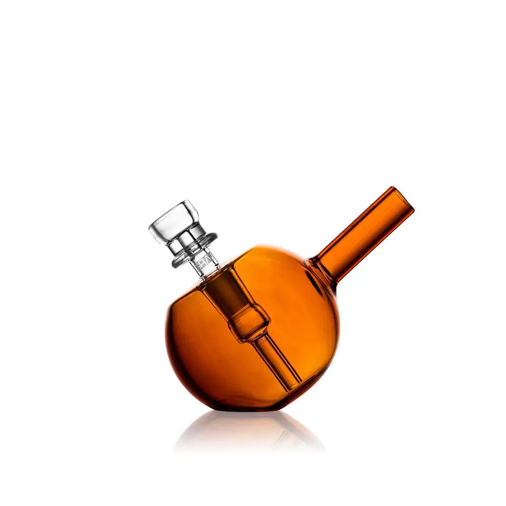 A close-up, slightly angled shot of a spherical amber glass bubbler with a clear glass bowl and mouthpiece, reflecting on a white surface.