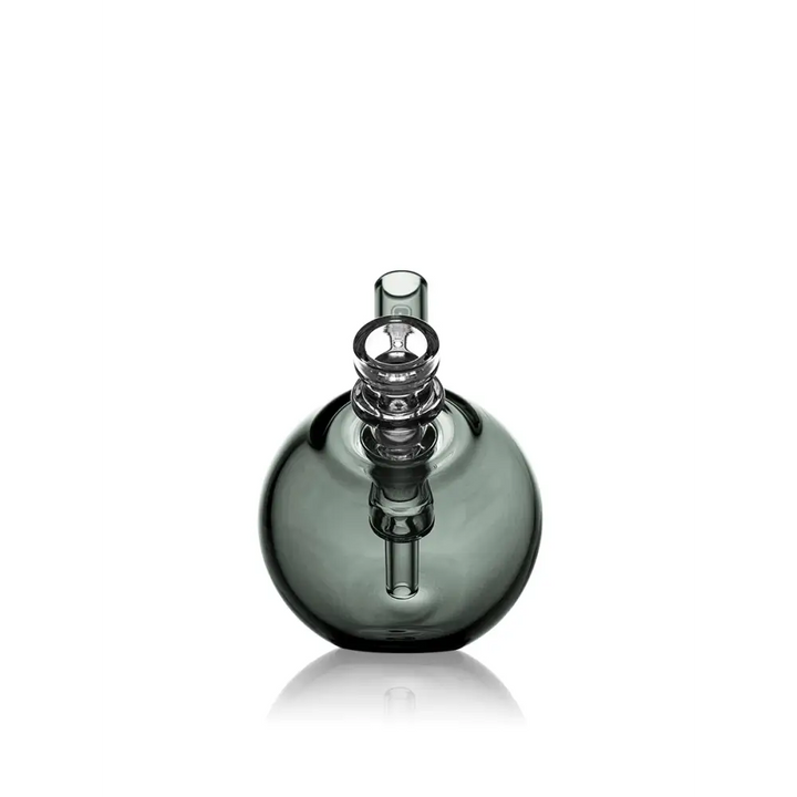 A compact, spherical dark gray glass bubbler with a clear glass joint and mouthpiece, reflecting on a pristine white surface.