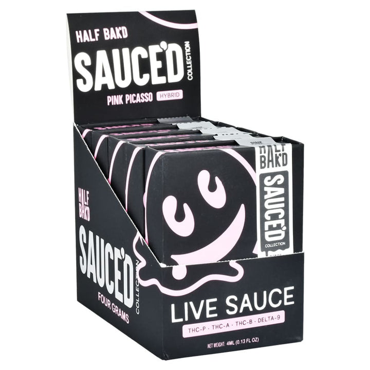 Close-up of a black display box filled with individual black product boxes, featuring pink and white branding for 'Half Bak'd Sauced'.