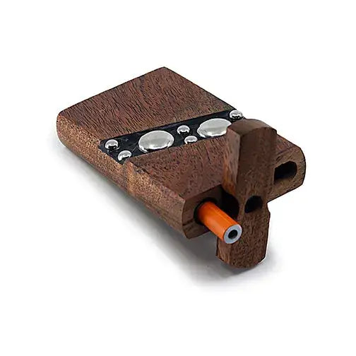 Close-up, angled view of a dark brown wooden dugout, featuring a row of large, shiny silver studs embedded on its top surface. An orange-tipped one-hitter pipe is partially visible, inserted into a compartment on the side.
