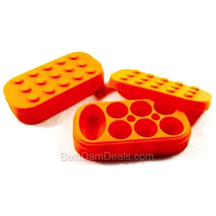 Three bright orange silicone containers, two with Lego-style studded tops and one with multiple circular compartments, arranged on a white surface.