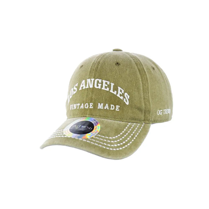 A light olive green baseball cap with 'LOS ANGELES' and 'VINTAGE MADE' embroidered in white on the front, featuring a holographic sticker on the brim.