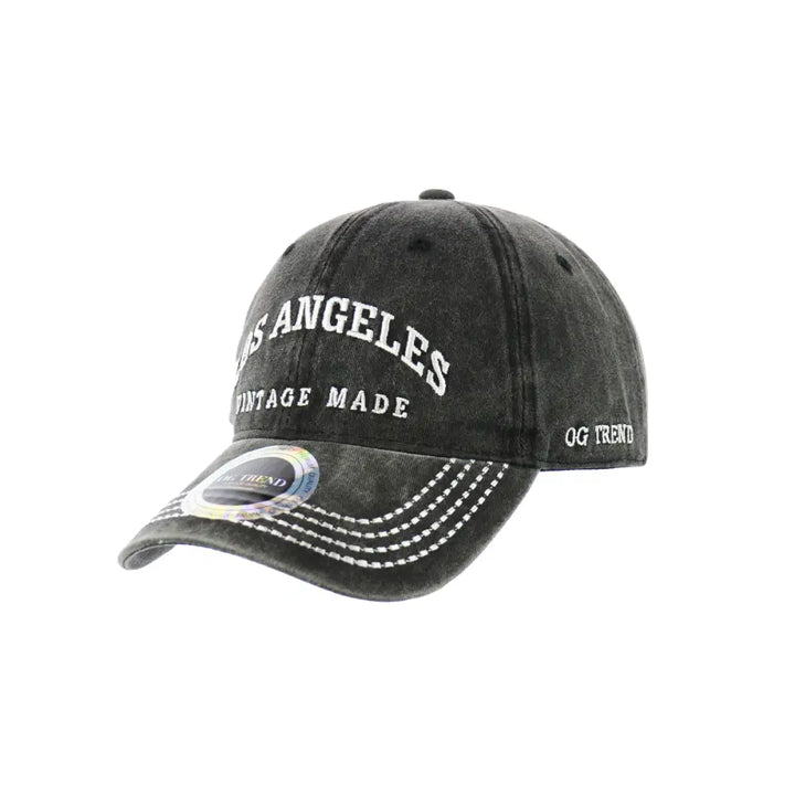 Slightly angled view of a distressed dark grey baseball cap featuring white embroidered 'LOS ANGELES' text and a holographic sticker on the brim.