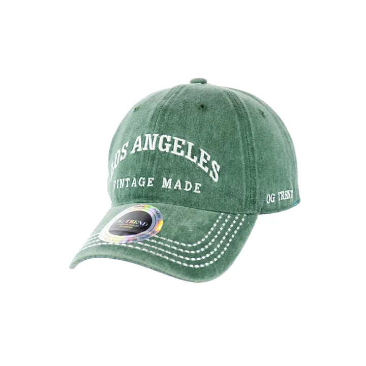 Close-up, slightly angled view of a distressed green baseball cap with 'Los Angeles Vintage Made' embroidered in white on the front, and white stitching on the brim.