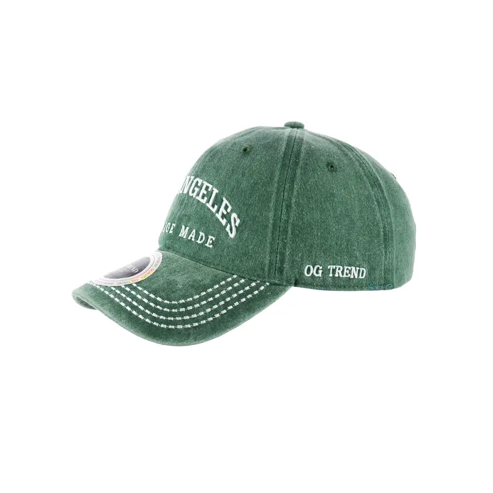 Close-up, angled view of a distressed green baseball cap with 'ANGELES' and 'MADE' embroidered in white on the front, and 'OG TREND' on the side.