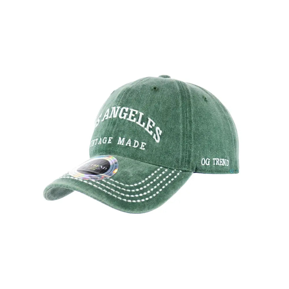 Close-up, angled view of a faded green baseball cap featuring 'LOS ANGELES' and 'VINTAGE MADE' embroidered in white on the front, with 'OG TREND' on the side and white stitching on the brim.