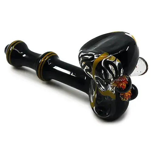 Angled close-up shot of a black glass hand pipe with yellow and orange marbled swirl patterns, showcasing its intricate design against a white background.