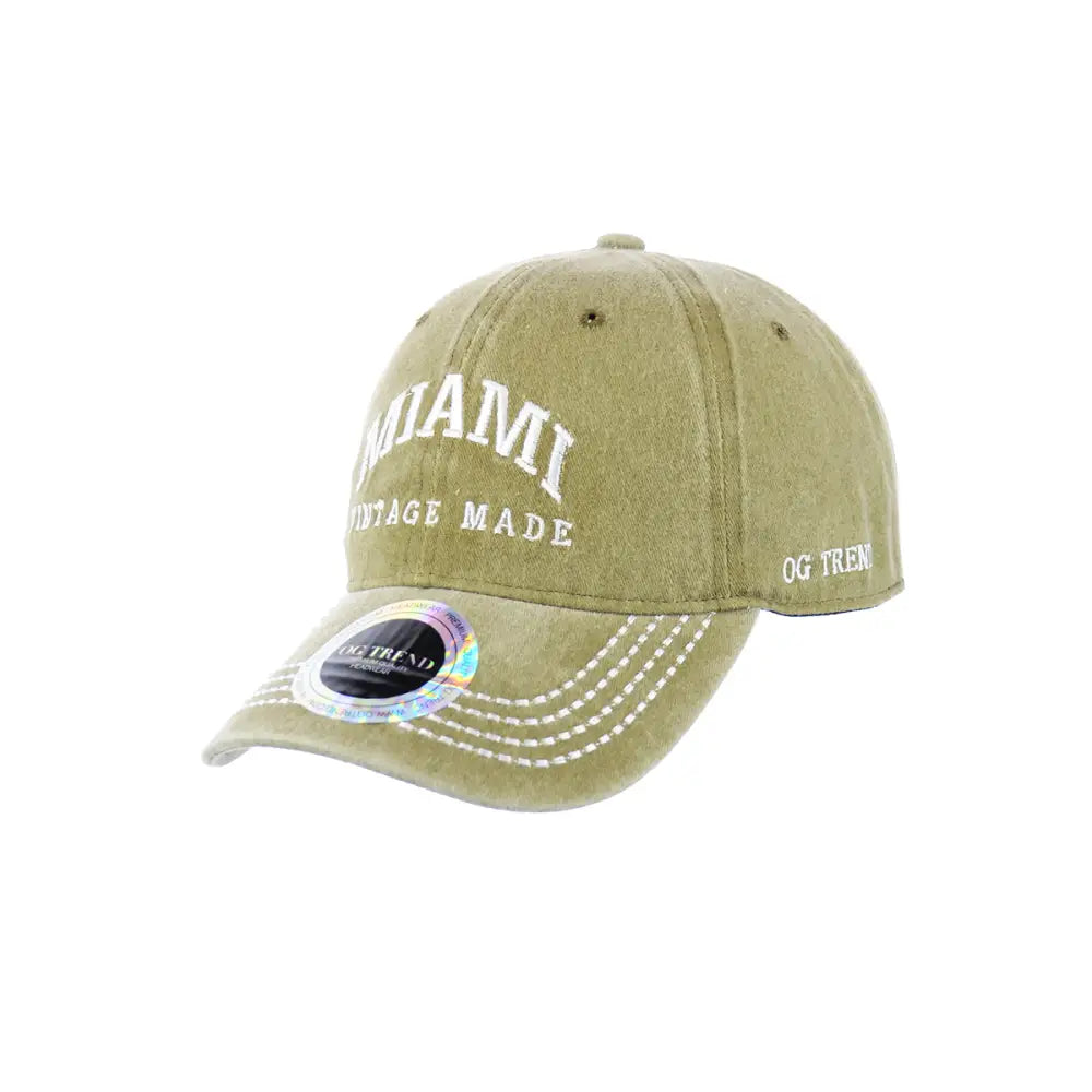 Front view of a distressed olive green baseball cap with 'MIAMI VINTAGE MADE' embroidered in white on the front, and 'OG TREND' on the side. A holographic sticker is on the brim.