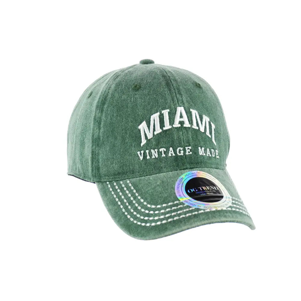 A faded green baseball cap with 'MIAMI' and 'VINTAGE MADE' embroidered in white on the front, featuring white stitching on the brim and a holographic sticker on the visor.