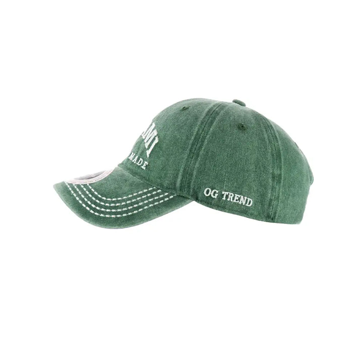 Side view of a distressed dark green baseball cap with white embroidered text 'MIAMI' on the front and 'OG TREND' on the side, featuring white stitching on the brim.