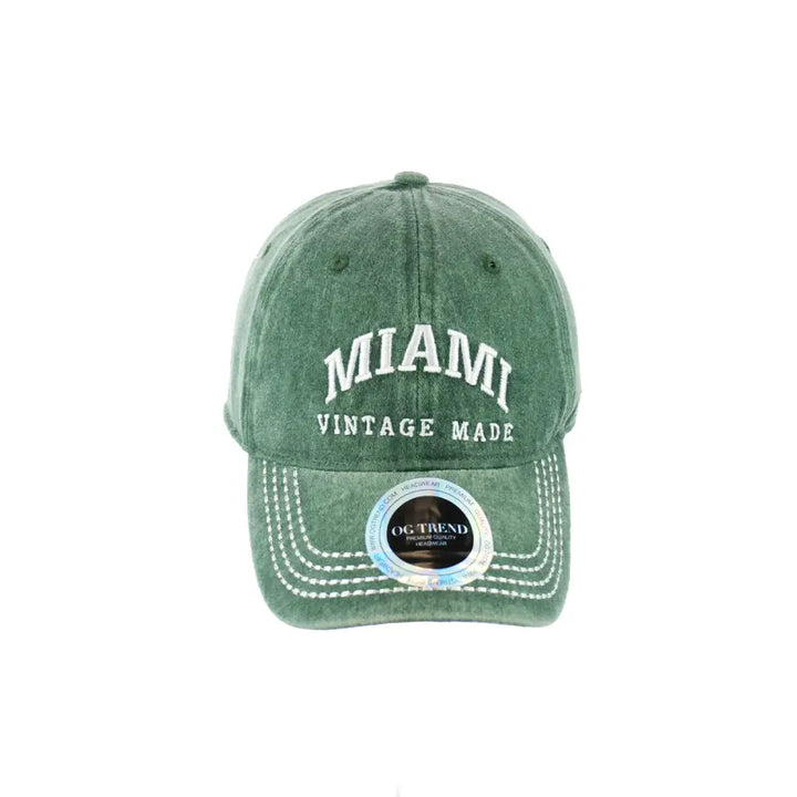 Front view of a distressed dark green baseball cap with 'MIAMI' and 'VINTAGE MADE' embroidered in white on the front, featuring visible white stitching on the brim.