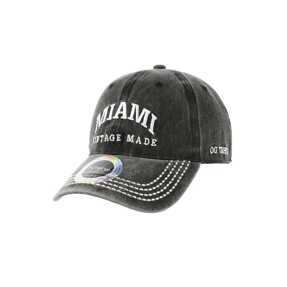 Close-up product image of a dark charcoal grey baseball cap with 'MIAMI' embroidered in white on the front, and 'VINTAGE MADE' below it. The brim has white stitching and a holographic sticker.