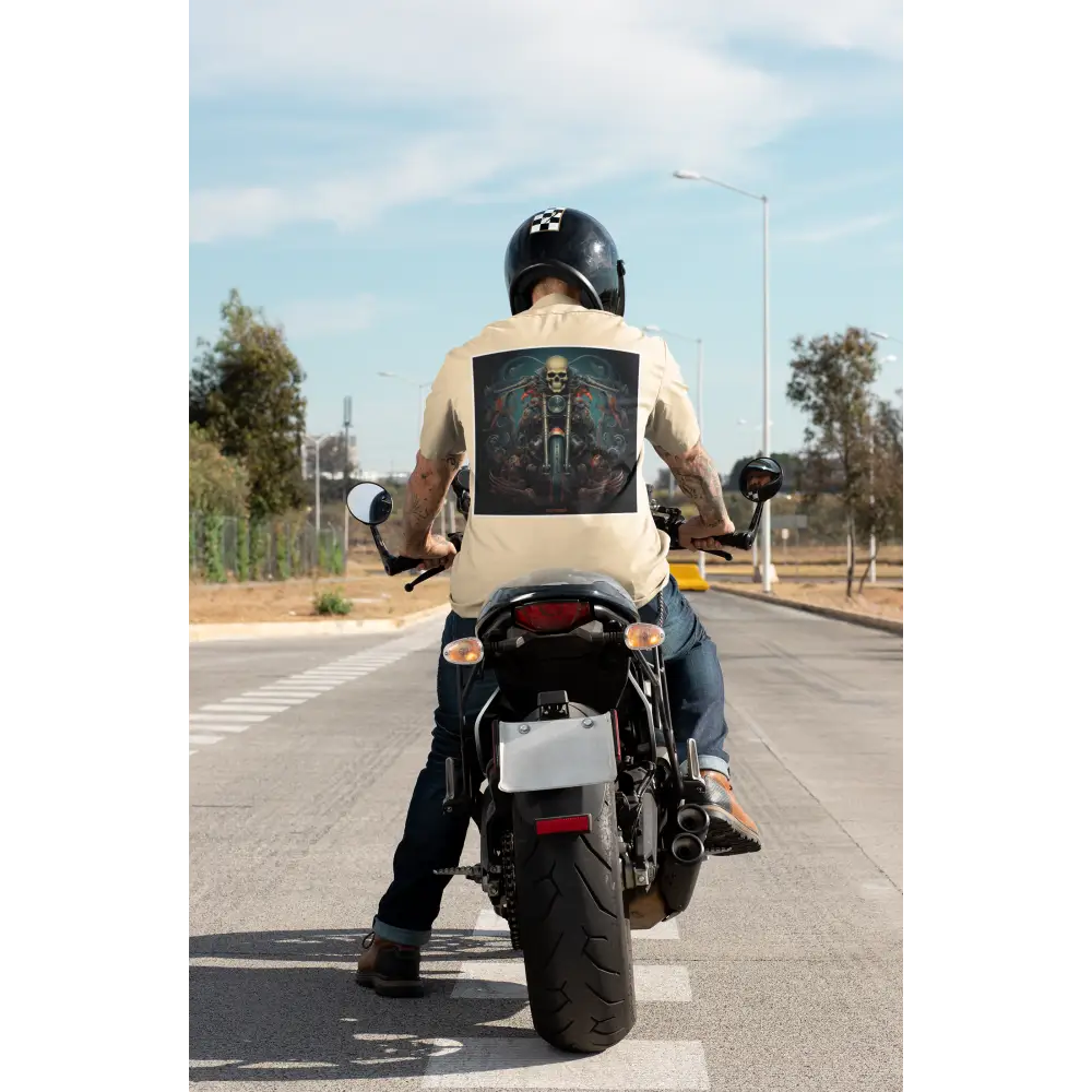 Rear view of a person wearing an off-white t-shirt with a skull and motorcycle graphic on the back, riding a black motorcycle on a paved road under a blue sky.
