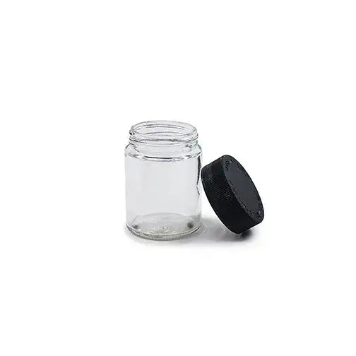 A small, clear glass jar with a black ribbed screw-on lid resting beside it on a clean white background.