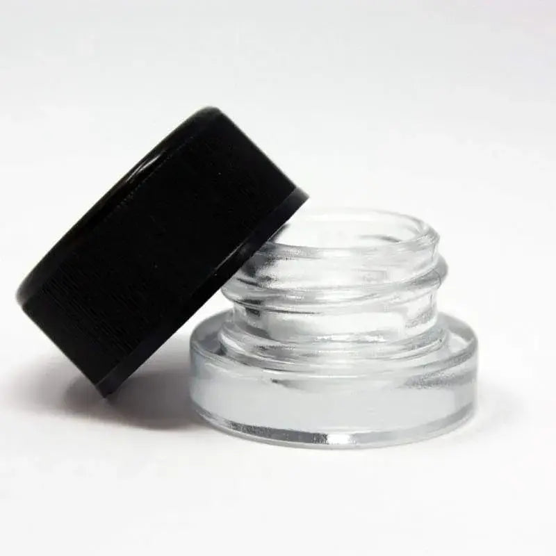 Detail shot of a small, clear glass jar with a black screw-on lid resting open beside it on a white surface.