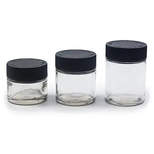 Three clear glass jars of varying sizes, each with a black screw-on lid, arranged in a row on a white surface.