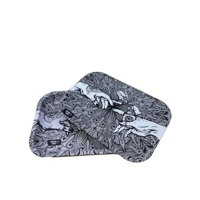 Two rectangular metal rolling trays with rounded corners, featuring a black and white design of hands passing a joint amidst intricate patterns, angled on a white background.